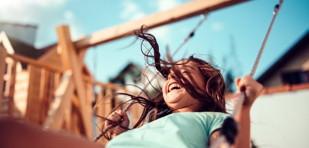 Photo portrait d'une petite fille heureuse assis sur une balançoire et souriant