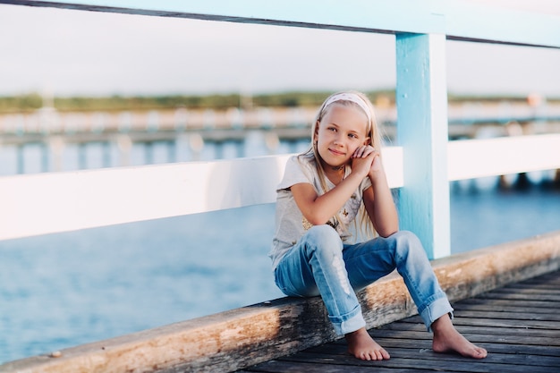 Portrait d'une petite fille heureuse assise sur un pont en bois avec la lumière du soleil.