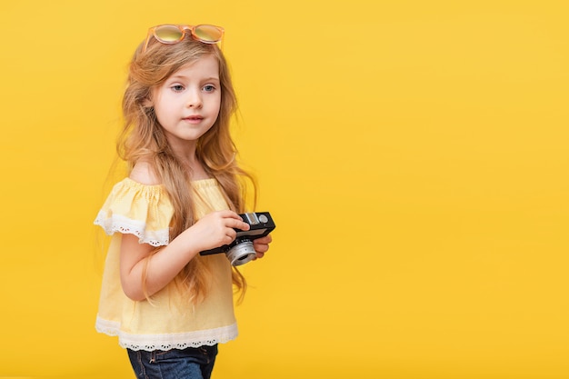 Portrait d'une petite fille heureuse aux cheveux longs avec un appareil photo rétro dans ses mains