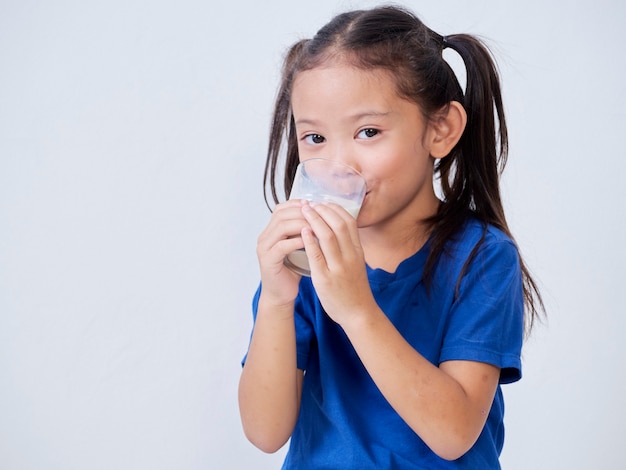 Portrait de petite fille heureuse, boire du lait de verre sur la lumière