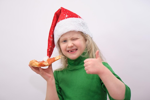 Portrait de petite fille heureuse avec bonnet de noel manger de la pizza sur fond blanc