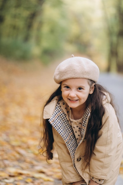 Portrait d'une petite fille heureuse en manteau beige et béret tenant des feuilles d'érable jaunes et passant du temps dans le parc d'automne