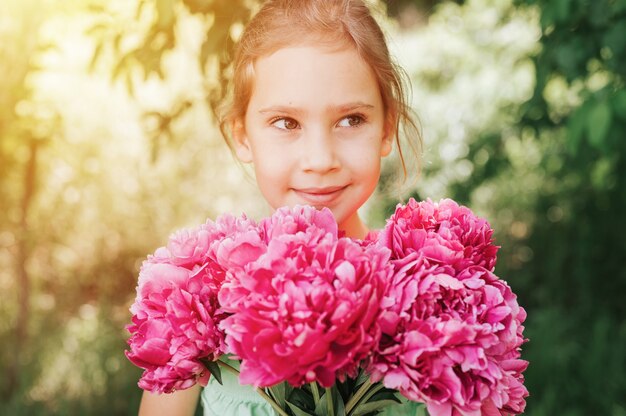 Portrait d'une petite fille heureuse de race blanche de sept ans, tient dans les mains un bouquet de pivoine rose