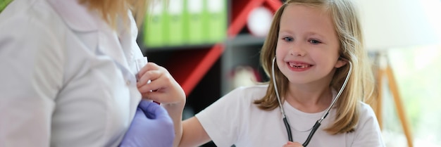 Portrait d'une petite fille joyeuse appliquant un stéthoscope médical lors d'un rendez-vous chez le médecin