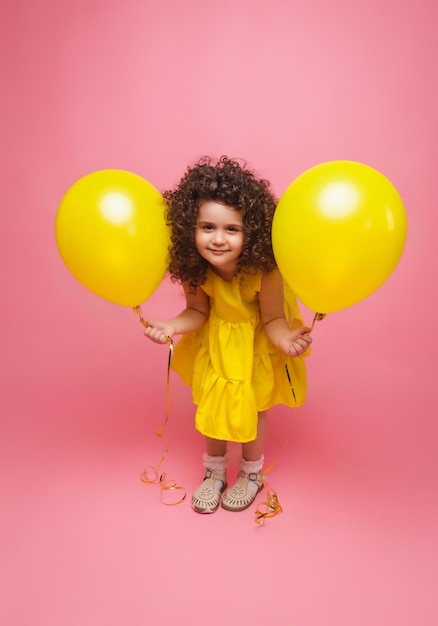 Portrait d'une petite fille joyeuse isolée sur fond rose tenant un bouquet de ballons colorés posant