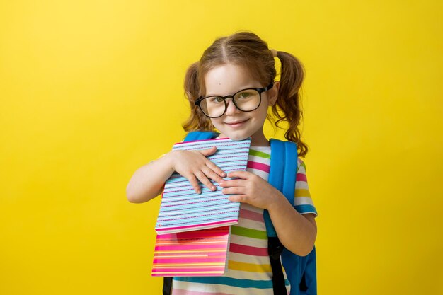 Portrait de petite fille avec des lunettes dans un t-shirt rayé avec des cahiers et des manuels et un sac à dos