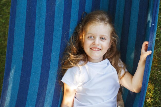 Portrait d'une petite fille mignonne aux cheveux longs reposant sur un hamac dans le jardin et souriant