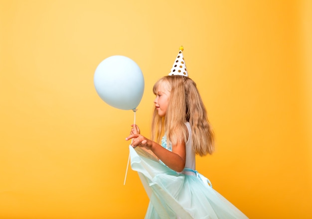 Portrait d'une petite fille mignonne dans une casquette festive et avec des ballons sur fond jaune.