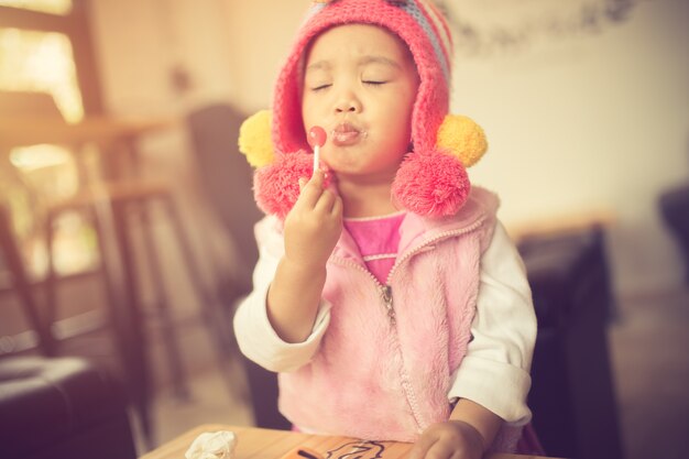 Portrait d&#39;une petite fille mignonne dans une robe rose, mangeant un rouge vif Lollipop debout