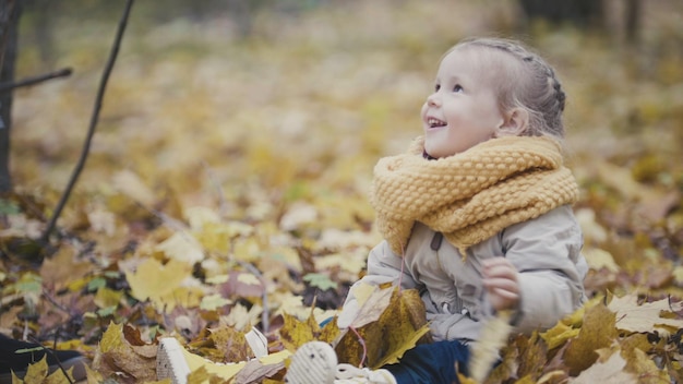Portrait de petite fille mignonne heureuse joue dans le parc d'automne parmi les feuilles jaunes