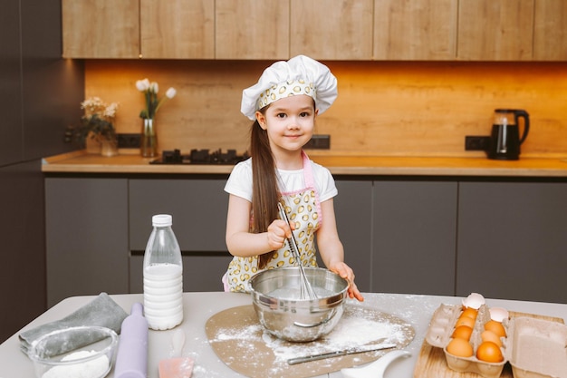 Portrait d'une petite fille mignonne se tenant dans une cuisine moderne et préparant la pâte