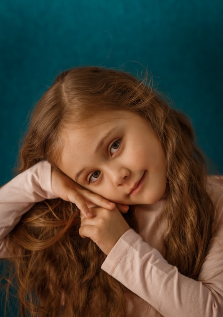 Portrait d'une petite fille pensive aux cheveux longs sur fond bleu