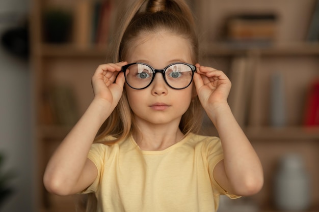 Portrait de petite fille portant des lunettes assis dans la bibliothèque