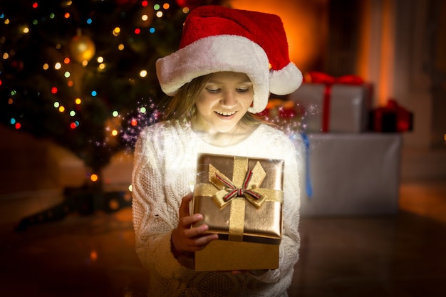 Portrait de petite fille posant avec une boîte cadeau dorée brillante