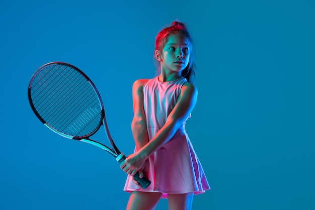 Portrait de petite fille s'entraînant au tennis, debout avec une raquette isolée sur fond bleu en néon