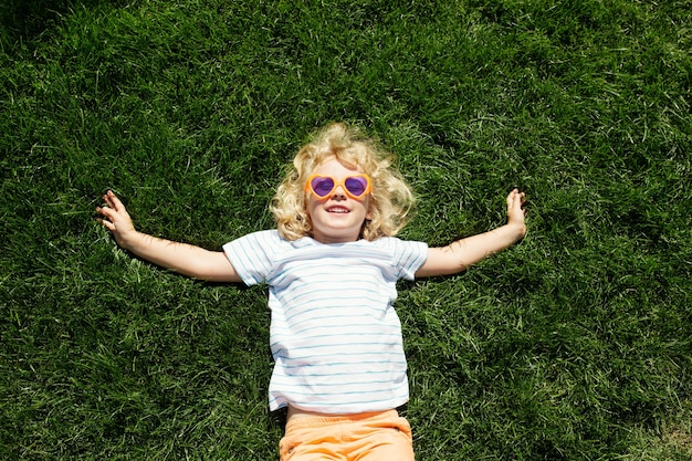 Portrait d'une petite fille souriante dans des lunettes de soleil en forme de coeur allongé