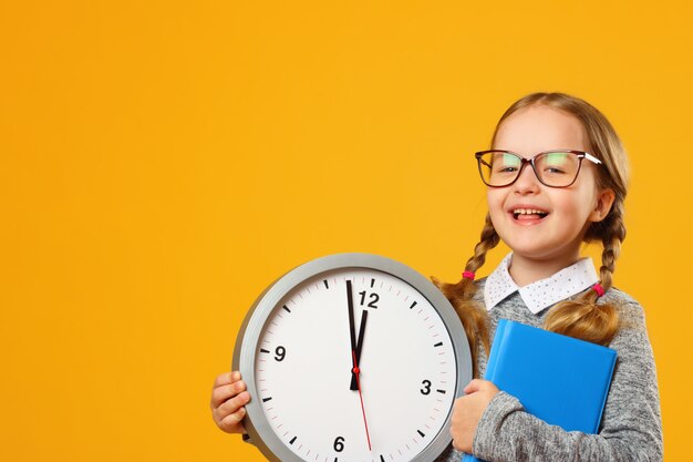 Portrait d&#39;une petite fille souriante à lunettes avec un livre et une horloge.