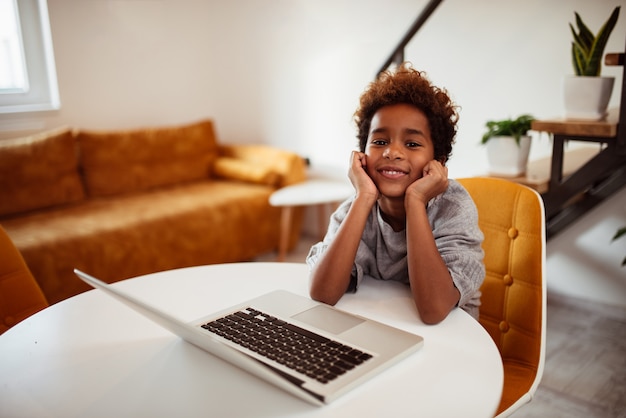 Portrait d&#39;une petite fille souriante avec ordinateur portable à la maison, regardant la caméra.