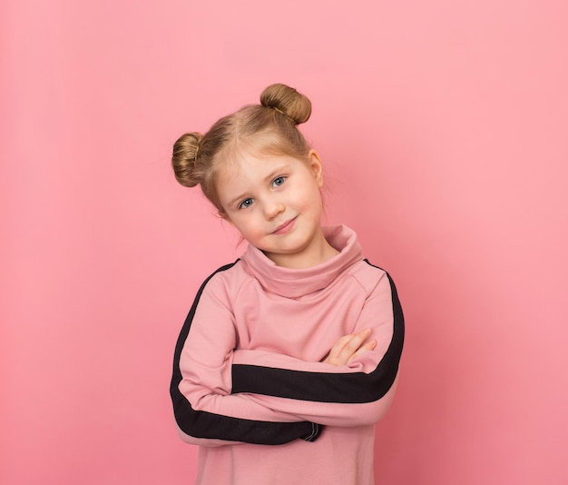 Portrait de petite fille souriante portant deux petits pains sur fond rose Enfant confiant avec les bras croisés