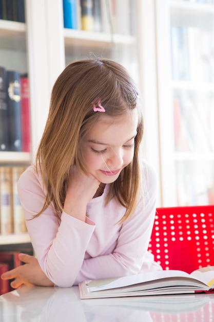 Portrait de petite fille souriante à table en lisant un livre