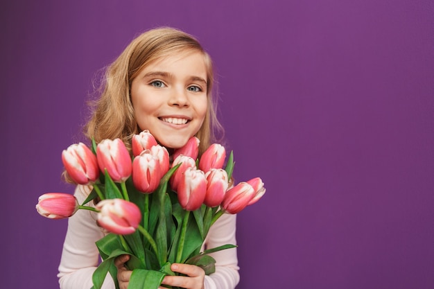 Portrait d'une petite fille souriante tenant un bouquet de tulipes isolées sur un mur violet