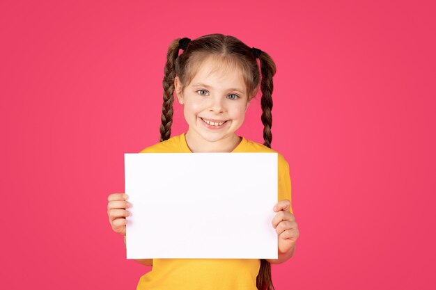 Portrait d'une petite fille souriante tenant une pancarte blanche vierge dans les mains