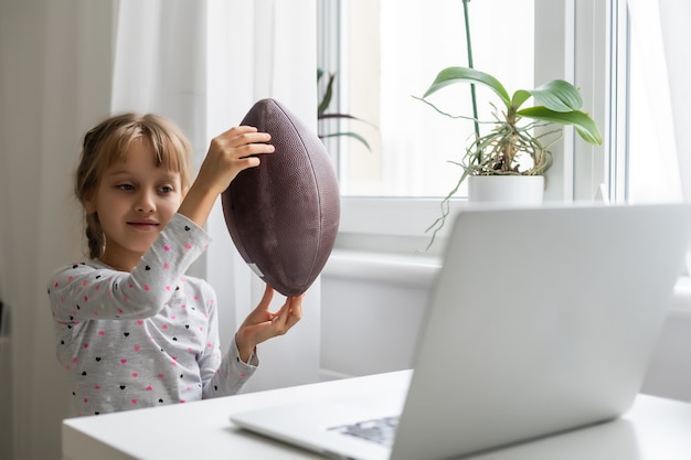 portrait de petite fille sportive avec ballon de rugby en regardant un ordinateur portable