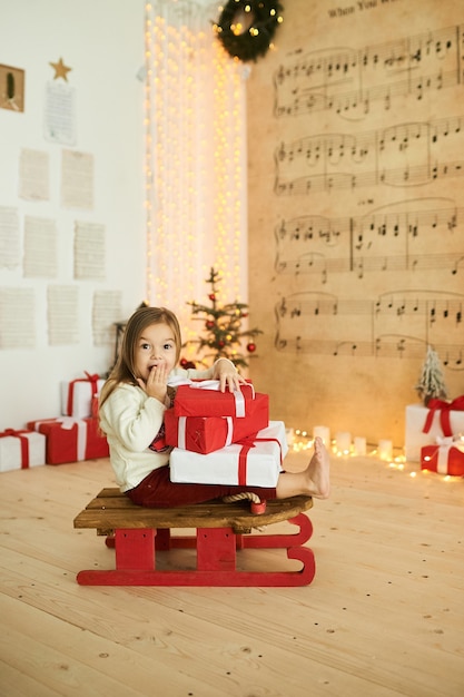 Portrait d'une petite fille sur un traîneau rouge avec un cadeau sur un fond de lumières floues