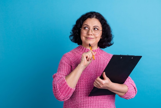 Portrait photo d'une femme d'affaires d'âge mûr senior concentrée garder la lecture du presse-papiers isolée sur fond de couleur bleue