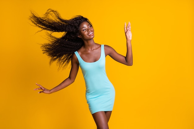 Portrait photo d'une femme afro-américaine rêveuse avec des cheveux volant un vent doux soufflant vêtue d'une robe bleue isolée sur fond de couleur jaune vif