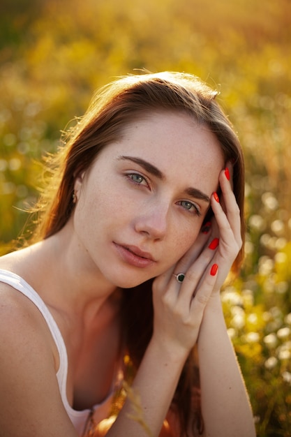 Portrait photo d'une femme au coucher du soleil Photo d'été d'une femme dans un champ de fleurs sauvages Golden time Closeup photo mains près du visage Femme avec des taches de rousseur