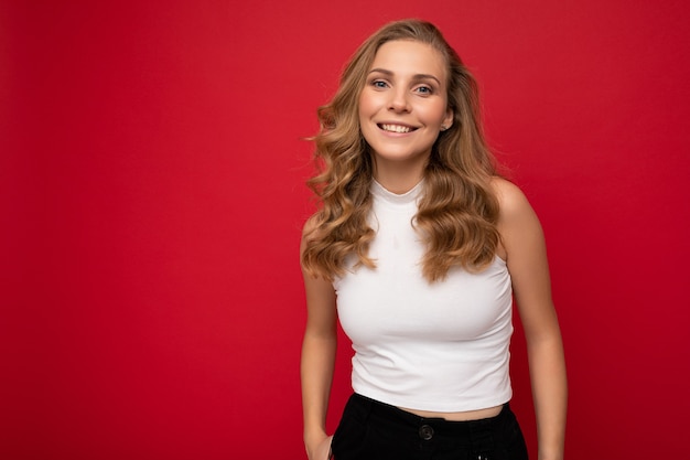 Portrait photo d'une femme blonde charmante, charmante et séduisante, souriante et souriante, avec des émotions sincères, portant des vêtements élégants isolés sur fond rouge avec espace de copie.