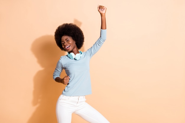 Portrait photo d'une fille afro-américaine insouciante dansant avec un poing dans l'air isolé sur fond de couleur beige pastel