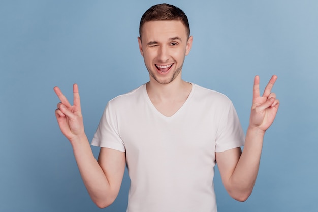 Portrait photo de l'homme positif heureux montrant v-sign geste souriant clin d'oeil isolé sur fond de couleur bleu pastel