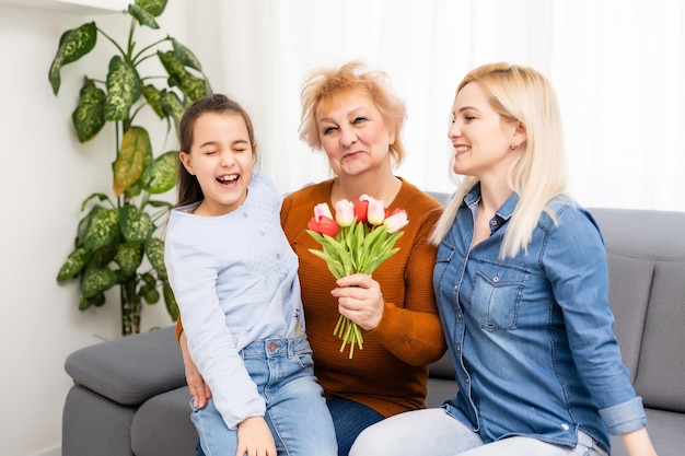 Portrait photo de petite-fille félicitant mamie donnant un bouquet de tulipes assis près de maman.