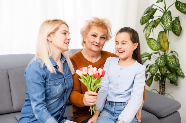 Portrait photo de petite-fille félicitant mamie donnant un bouquet de tulipes assis près de maman.