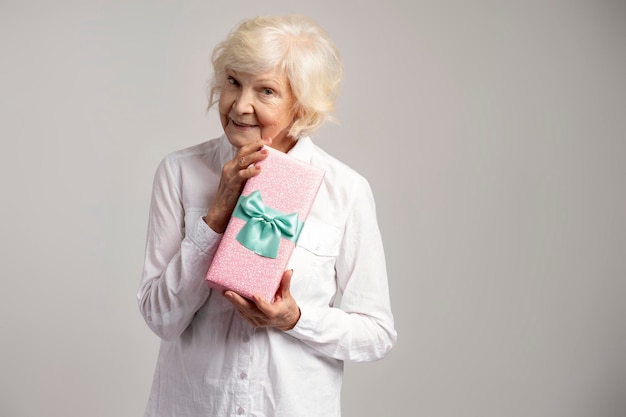 Portrait photo d'une vieille dame curieuse tenant une boîte présente et souriante isolée sur fond gris Concept de la journée de la femme