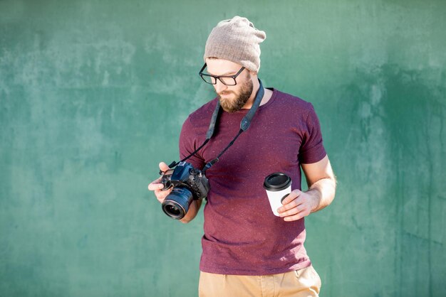 Portrait d'un photographe élégant habillé décontracté en t-shirt et chapeau debout avec caméra sur fond vert