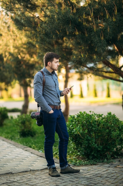 Portrait de photographe professionnel à l'extérieur. L'homme utilise le meilleur appareil photo et le meilleur bracelet en cuir. Beau jeune homme confiant en chemise, debout contre la rue.