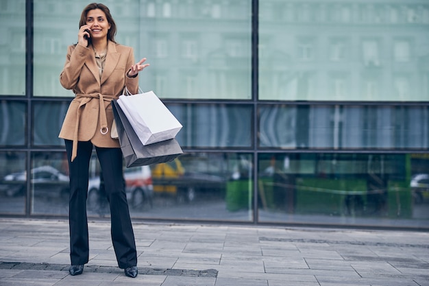 Portrait en pied d'une belle jeune femme caucasienne gaie parlant au téléphone portable à l'extérieur