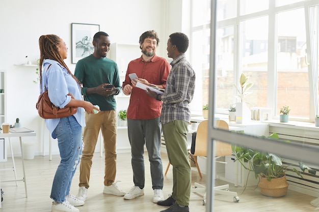 Photo portrait en pied d'un groupe multiethnique de personnes vêtues de vêtements décontractés et souriant joyeusement tout en discutant du travail debout au bureau