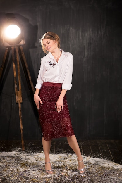 Portrait en pied d'une jeune femme élégante en jupe rouge, crayon, chemisier blanc et talons hauts. Studio de mode tourné sur fond noir. Robe de soirée ou concept de robe de fête