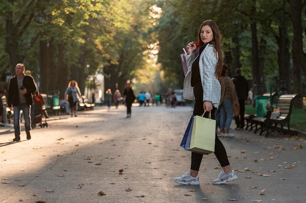 Portrait en pied d'une jeune femme avec des sacs à provisions en papier marchant dans le parc