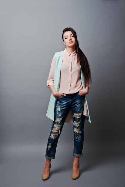 Portrait en pied jeune fille brune vêtue d'une blouse rose, d'une veste turquoise, d'un jean déchiré et de chaussures crème