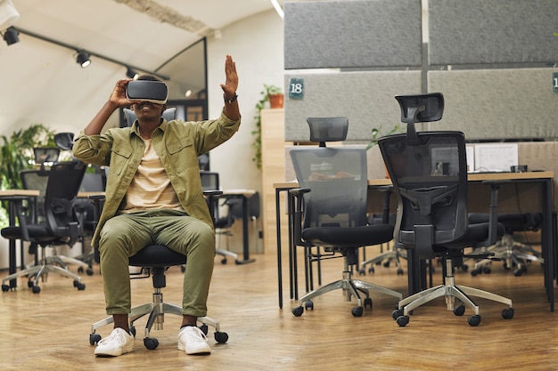 Portrait en pied d'un jeune homme afro-américain portant des vêtements de réalité virtuelle au bureau et profitant de la réalité immersive, copiez l'espace