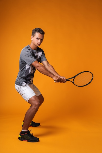 Portrait en pied d'un joueur de tennis homme en action sur fond orange close up