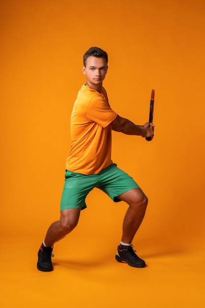 Portrait en pied d'un joueur de tennis homme en action sur fond orange close up