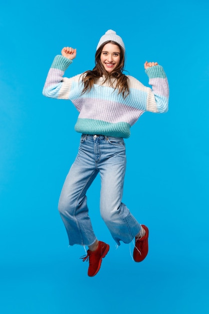 Portrait en pied vertical fille super heureuse sautant d'étonnement, célébrant le nouvel an, fête de Noël, profitant des vacances, faisant du shopping avec des remises impressionnantes, souriant optimiste, fond bleu