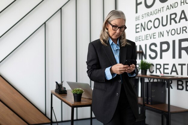 Portrait d'une pigiste adulte mature aux cheveux gris tenant un téléphone à l'intérieur