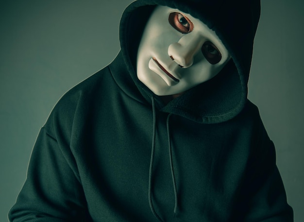 Portrait d'un pirate anonyme portant un masque et un sweat à capuche noir assis la tête inclinée et terrifiante Concept de piratage et de malware